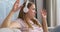 A young Caucasian woman wearing wireless headphones sits on a couch at home