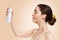 A young Caucasian woman, with wet skin, holding a bottle of cosmetics. Copy space. Side view. Beige background. Concept of