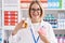 Young caucasian woman working at pharmacy drugstore holding pills an piggy bank smiling with a happy and cool smile on face