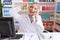 Young caucasian woman working at pharmacy drugstore speaking on the telephone doing peace symbol with fingers over face, smiling