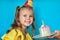 Young celebrating girl blowing candle on a piece of cake on blue background. Copy space