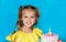 Young celebrating girl smile while her mom`s hand holding a piece of cake on blue background. Copy space