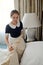 Young chambermaid straightening pillows on double bed with clean bedclothes