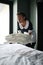 Young chambermaid in uniform putting stack of clean folded sheets on bed