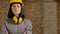 Young charming builder woman standing in earphones, glasses and helmet with crossed hands looking in camera, brick