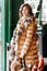 Young charming girl dressed in beige knit dress and a light brown down jacket with fur poses in the street