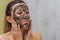 Young charming girl makes a black charcoal mask on her face