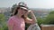 Young charming townswoman is sitting on hill against panorama of city in sunny day