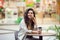 Young cheerfful woman using smartphone and drinking take away coffee in paper cup. Stylish woman sitting at cafe indoors