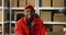 Young cheerful African American postman in red iniform and cap sitting at desk in postal office store and working at