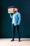 Young cheerful, bearded, hipster man, dressed in denim shirt, stands indoors, holding wooden box