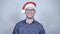 Young cheerful businessman in santa claus hat smiling over grey background.