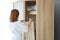 Young cheerful caucasian woman in white pajama choosing clothes in wardrobe in bedroom with happy face life style and relaxation