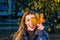 Young cheerful cute girl woman playing with fallen autumn yellow leaves in the park near the tree, laughing and smiling