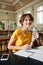 Young cheerful female student with water in hand happily looking in camera while study in library of university