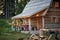 Young cheerful friends in front of wooden cottage on the terrace.  Guy and girl playfully fighting over beer. Girl playing guitar