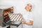 Young cheerful girl confectioner in the pastry workshop, holding the baking tray with white macarons cookies before