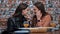 Young and cheerful girls gossip and whisper to each other while sitting in a cafe.