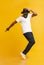 Young cheerful man dancing on tiptoes on yellow studio background