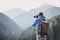 Young cheerful man photographer taking photographs with digital camera in a mountains.