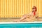 A young cheerful woman with African pigtails sits on the edge of a sunbathing pool.