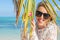 Young cheerful woman on the beach hiding behind palm leaf