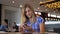 Young Cheerful Woman In Blue Checkered Shirt Sits In Cafe Uses Smartphone