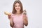 Young and cheerful woman hold yellow eclair and chocolate cake in hands. She look on camera. Isolated on grey background.