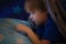 Young child boy age 3-5 playing on smart phone in bed under the bed covers at night. Real people
