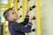 Young child boy exercising on a wall ladder bar inside sports gym room in a school