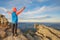 Young child boy hiker standing with raised hands in mountains enjoying view of amazing mountain landscape at sunset