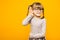 A young child girl journalist in glasses with funny pigtails listening to something holding his hand to ear