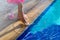 Young child girl in pink dress and shoes standing barefoot at the edge of a swimming pool try with her leg cool blue water,