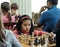 Young child making a move with a horse during a chess tournament at a school, with several other competitors in the background