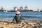 Young child sits on the Elbe beach in Hamburg with harbor and ships in the background