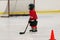 The young child wearing in red hockey equipment hockey helmet, skates, gloves. stick are playing hockey.