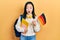 Young chinese girl exchange student holding germany flag afraid and shocked with surprise and amazed expression, fear and excited