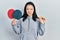 Young chinese girl holding red ping pong rackets and ball clueless and confused expression