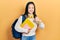 Young chinese girl holding student backpack and books doing happy thumbs up gesture with hand