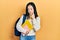 Young chinese girl holding student backpack and books pointing to the eye watching you gesture, suspicious expression