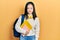 Young chinese girl holding student backpack and books skeptic and nervous, frowning upset because of problem