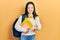 Young chinese girl holding student backpack and books smiling cheerful offering palm hand giving assistance and acceptance