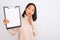 Young chinese inspector woman holding clipboard standing over isolated white background serious face thinking about question, very