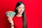 Young chinese woman holding australian dollars looking positive and happy standing and smiling with a confident smile showing