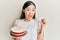 Young chinese woman holding carrot cake screaming proud, celebrating victory and success very excited with raised arms