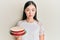 Young chinese woman holding carrot cake thinking attitude and sober expression looking self confident