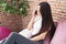 Young chinese woman talking on smartphone sitting on bed at bedroom