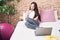 Young chinese woman talking on smartphone sitting on bed at bedroom