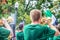 Young clean cut men in sweaty green t shirts play trumpets in parade with bokeh trees and American flag in background - back view