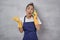 Young cleaning lady in uniform and rubber gloves playing with kitchen sponge, pretending talking on mobile phone while